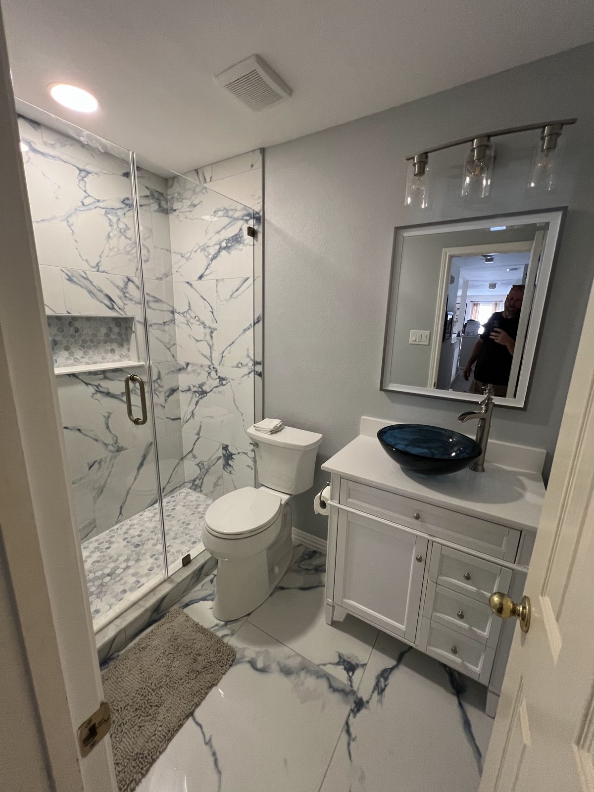Bathroom remodel with marble-look tile shower and glass vessel sink