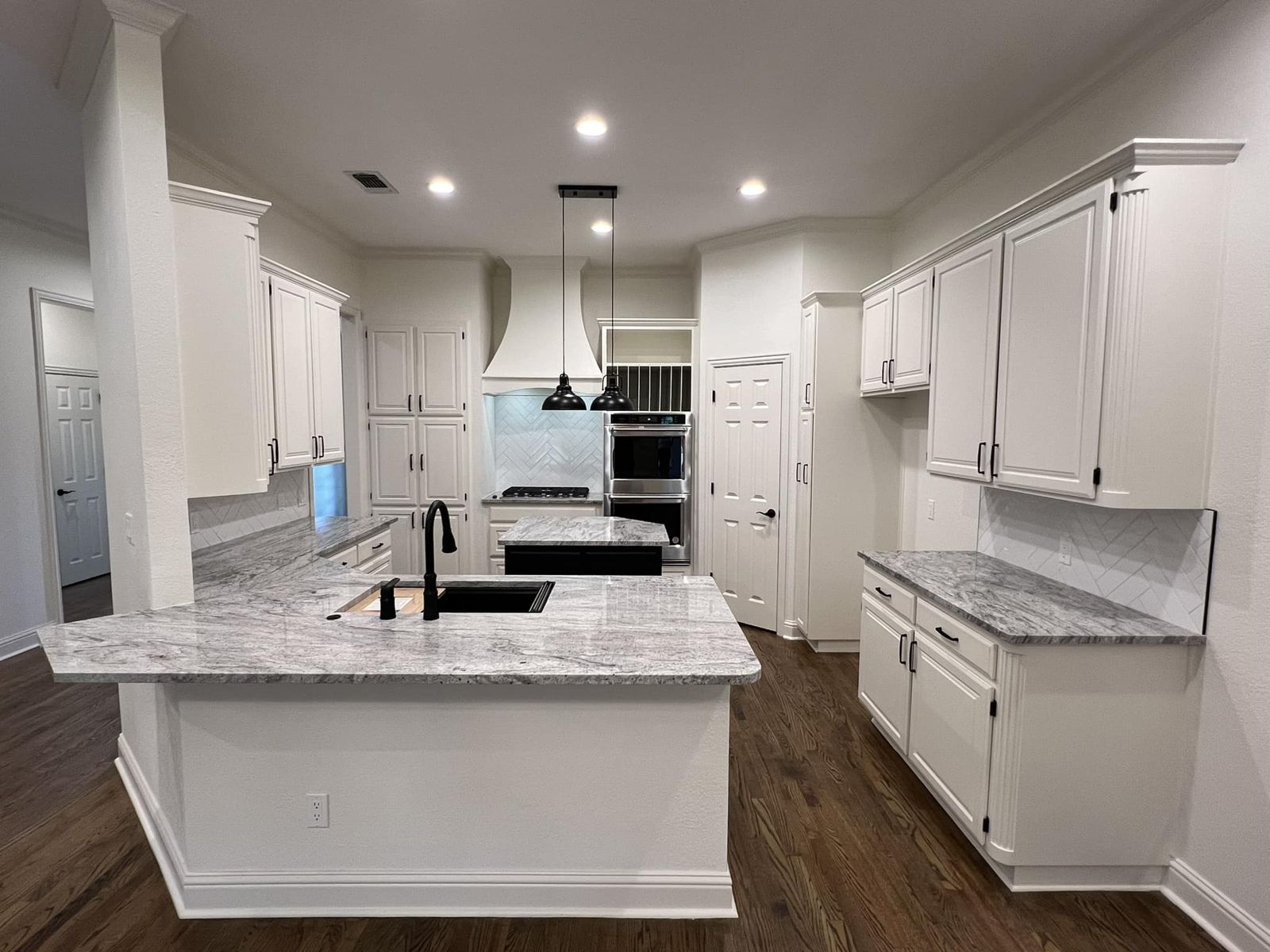 White kitchen with marble-look countertops, range hood and hardwood floors