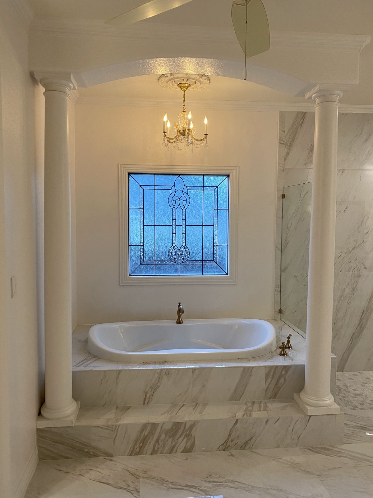 Master bathroom with soaking tub, columns, chandelier and marble-look tile