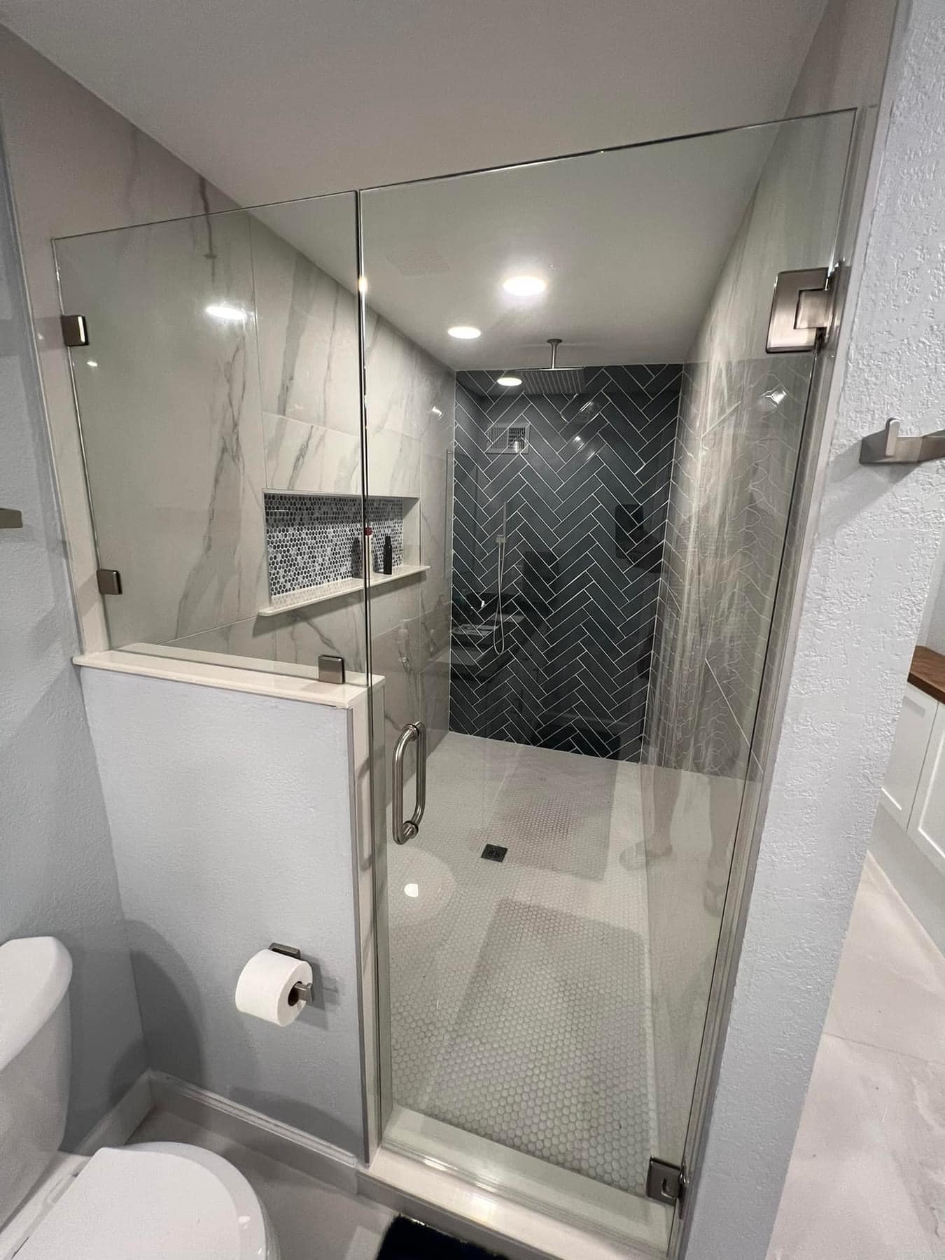 Custom shower with black herringbone tile and frameless glass door near TCU